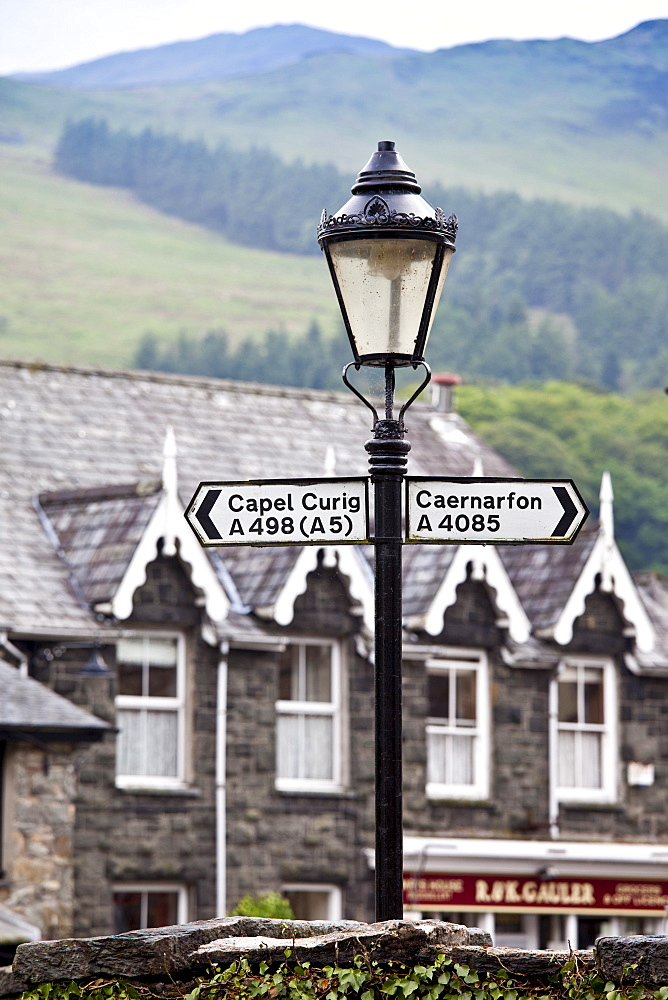 Signpost to Capel Curig and Caernarfon with Welsh slate roofs and mountains backdrop, Beddgelert, Gwynedd, Wales