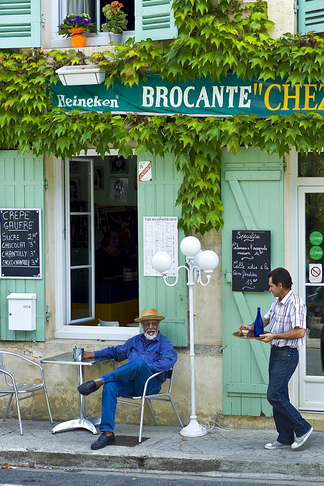 Waiter serves customer Pastis at traditional French Cafe in town of Castelmoron d'Albret in Bordeaux region, Gironde, France