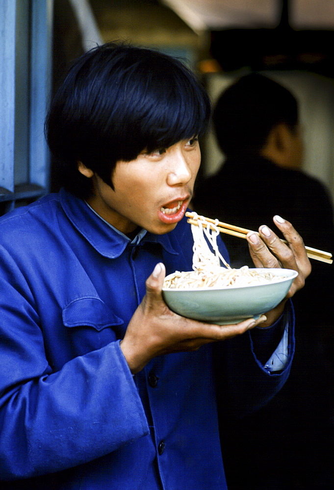 Chinese man wearing Chairman Mao jacket eating noodles with traditional chopsticks in China in the 1980s