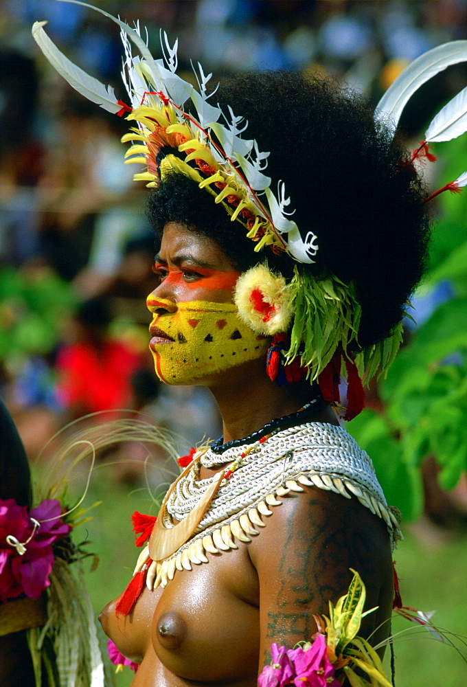 Bare-breasted native woman wearing a feathered headdress, beaded necklaces and face paints during  a gathering of tribes at Mount Hagen in Papua New Guinea