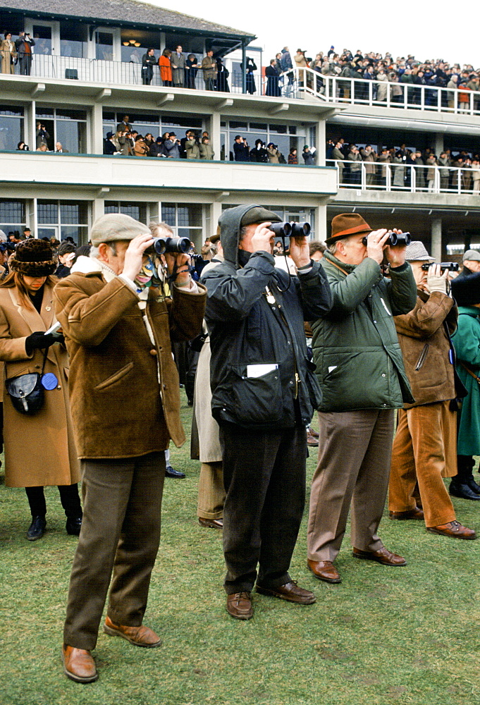 Spectactors with binoculars in front of grandstand at Cheltenham Racecourse for the National Hunt Festival of Racing, UK