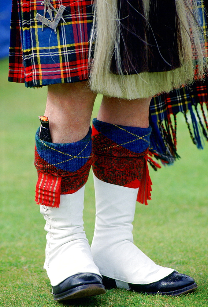 Scottish piper wearing tartan kilt, white gaiters, sporran and with dirk (knife) tucked in h is sock at the Braemar Games highland gathering  in Scotland.