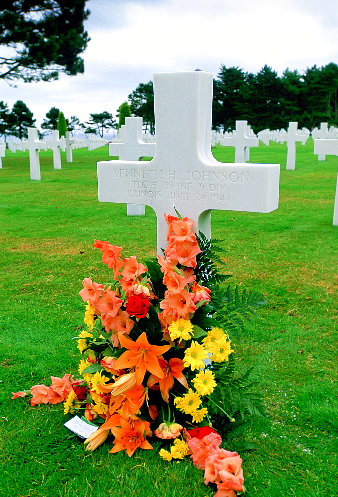 Headstones at a United States Military Cemetery at Utah Beach in Normandy, France.  Flowers have been left beside one of the crosses dedicated to a US serviceman.