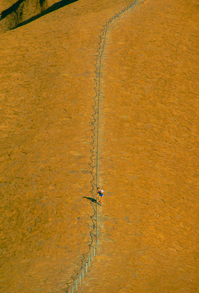 Tourist visiting Ayers Rock in Australia holds onto the roped handrail for support