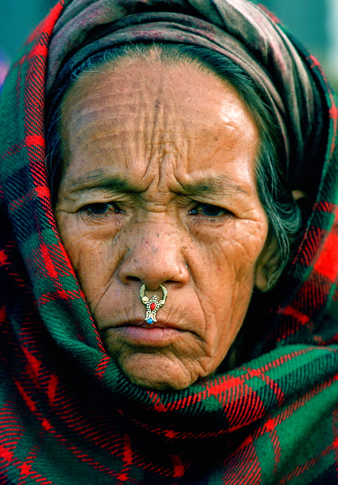 A woman from the Kathmandu valley in Nepal wearing nose jewels in the traditional way.  Her head is covered with a tartan shawl.