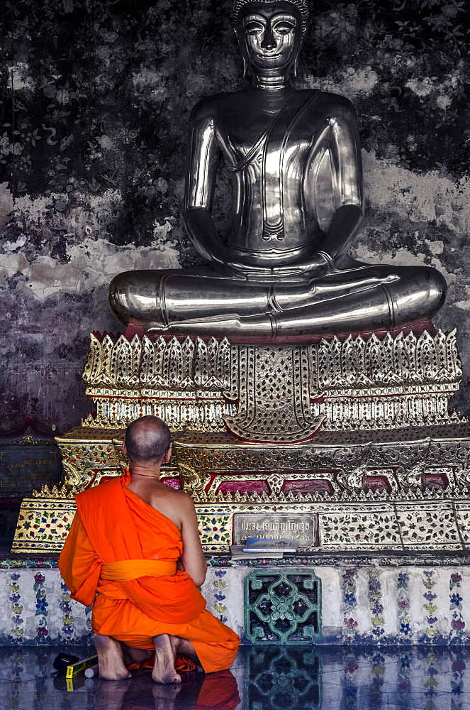 A monk prays in front of a golden Buddha, Wat Suthat, Bangkok, Thailand, Southeast Asia, Asia 