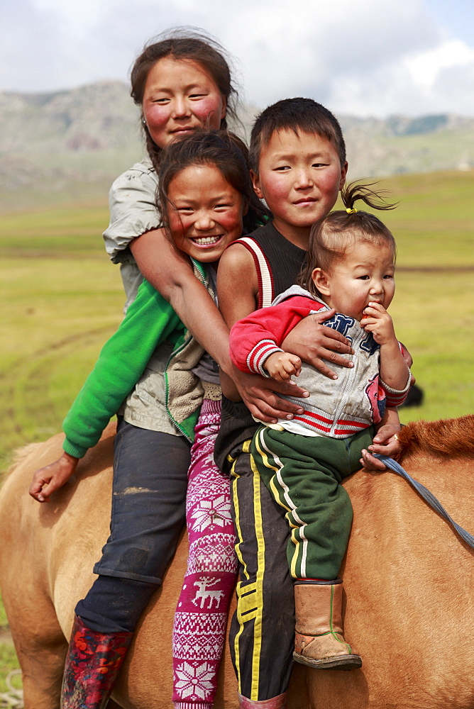 Portrait of four smiling and happy nomad siblings on their tame horse at summer nomad camp, Khujirt, Uvurkhangai, Central Mongolia, Central Asia, Asia