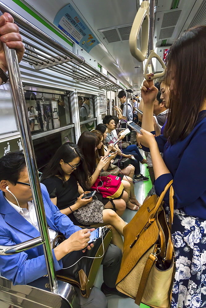 Smartly dressed commuters on the busy subway looking at their phones and e-devices, Seoul, South Korea, Asia