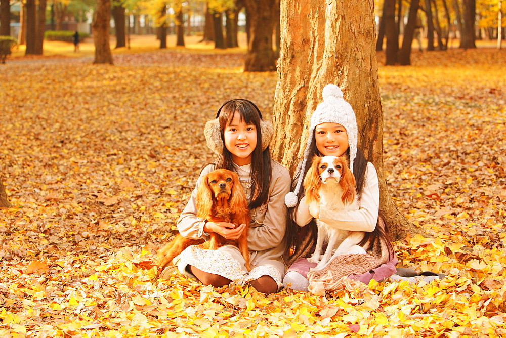 Girls Holding Their Dog In Leaves