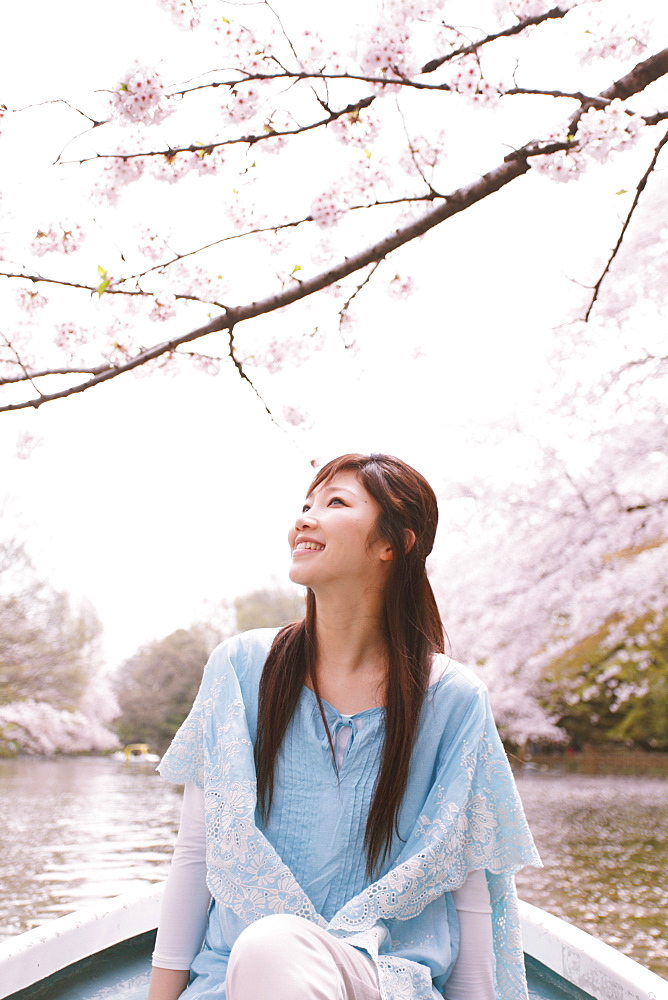 Woman In Rowing Boat On Lake With Cherry Blossom In Background