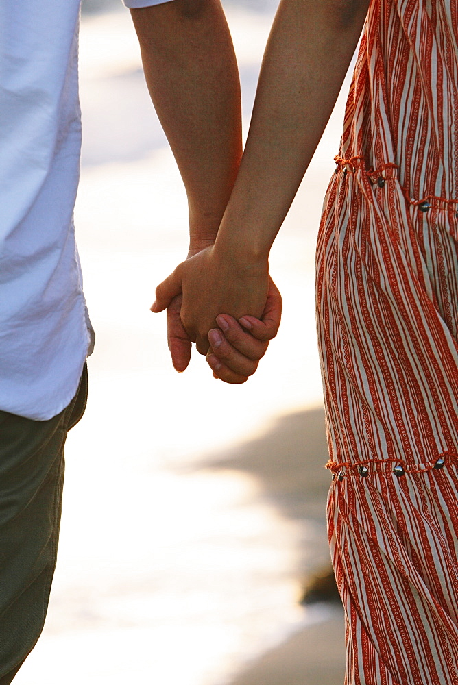 Close up of a couple holding hands by the beach