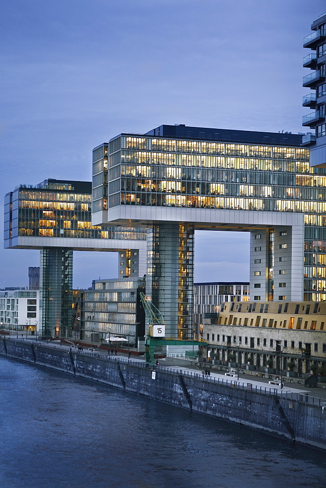 View of illuminated glass building with river at side in Rheinauhafen, Cologne, Germany