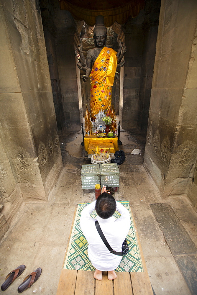 A man praying in front of a statue of Buddha, Angkor Wat, Siem Reap, Cambodia, Southeast Asia