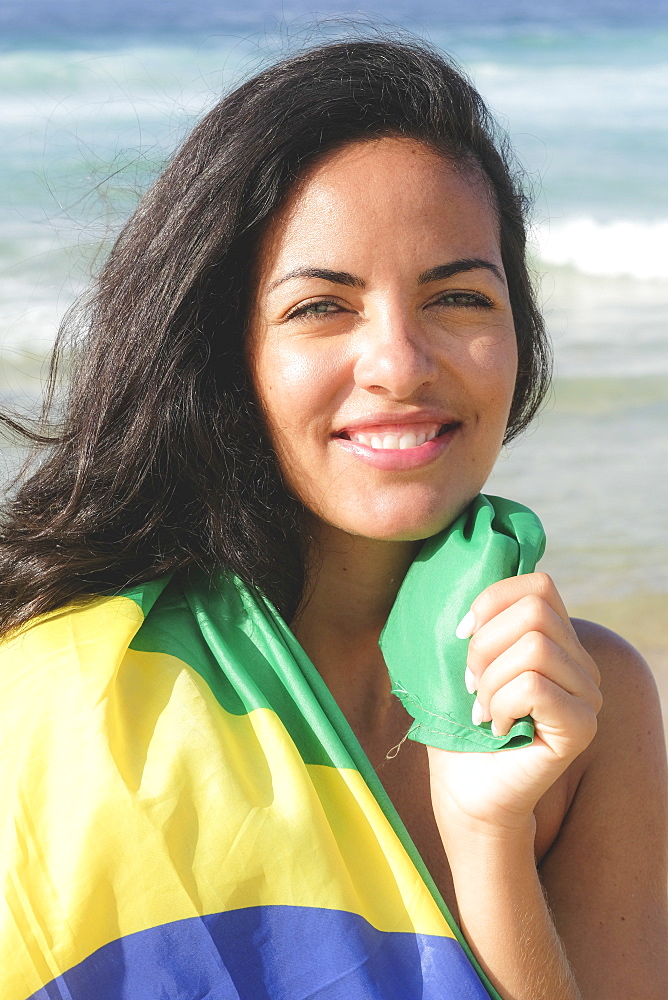 Young Brazilian woman, 20 to 29 years old, wrapped in the Brazilian flag on a beach in Rio de Janeiro, Brazil, South America