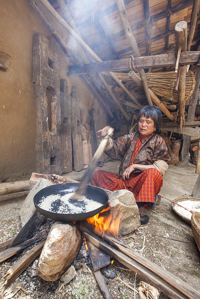 Old woman of Thimphu with traditional clothes cooking rice for lunch in a simple wooden house, Bhutan, Asia