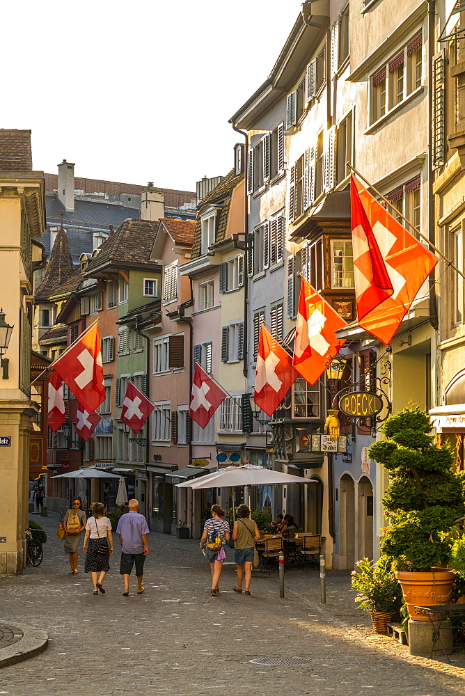 Tourists look at the Swiss flags hanging from buildings in Lindenhof, Zurich, Switzerland, Europe