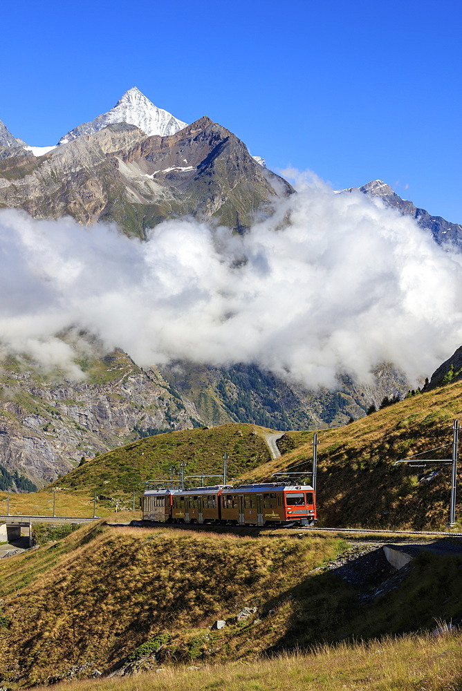 The red Bahn train proceeds with the peak of Dent Herens in the background, Gornergrat, Canton of Valais, Swiss Alps, Switzerland, Europe