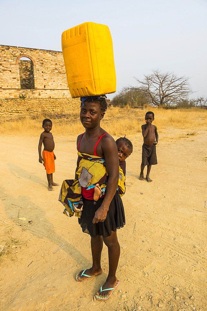 Woman with her baby on her back carrying a water canister on her head, Massangano, Cuanza Norte, Angola, Africa