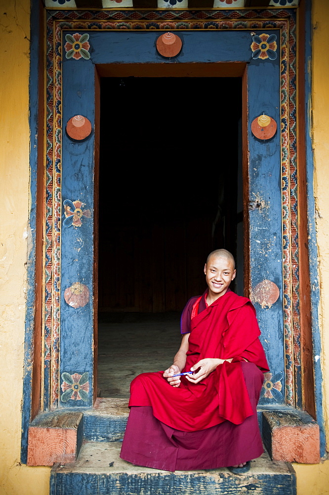 Young monk sitting in an ornate doorway, Punakha, Bhutan, Asia