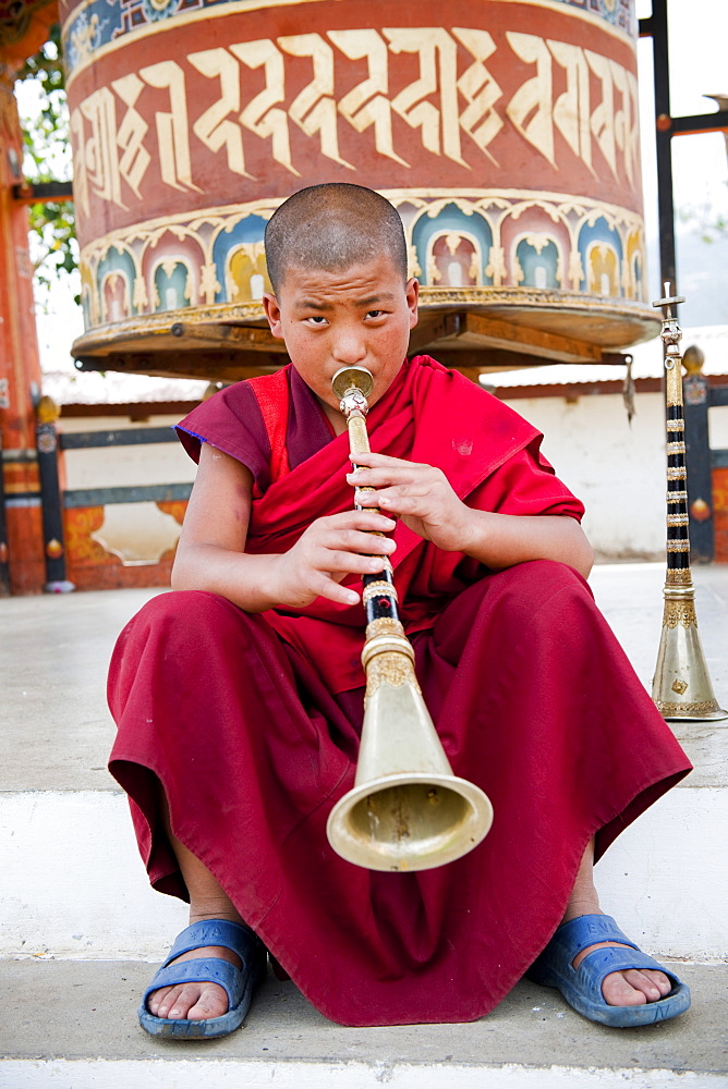 Monk playing lingum trumpet in front of a prayer wheel, Punakha, Bhutan, Asia