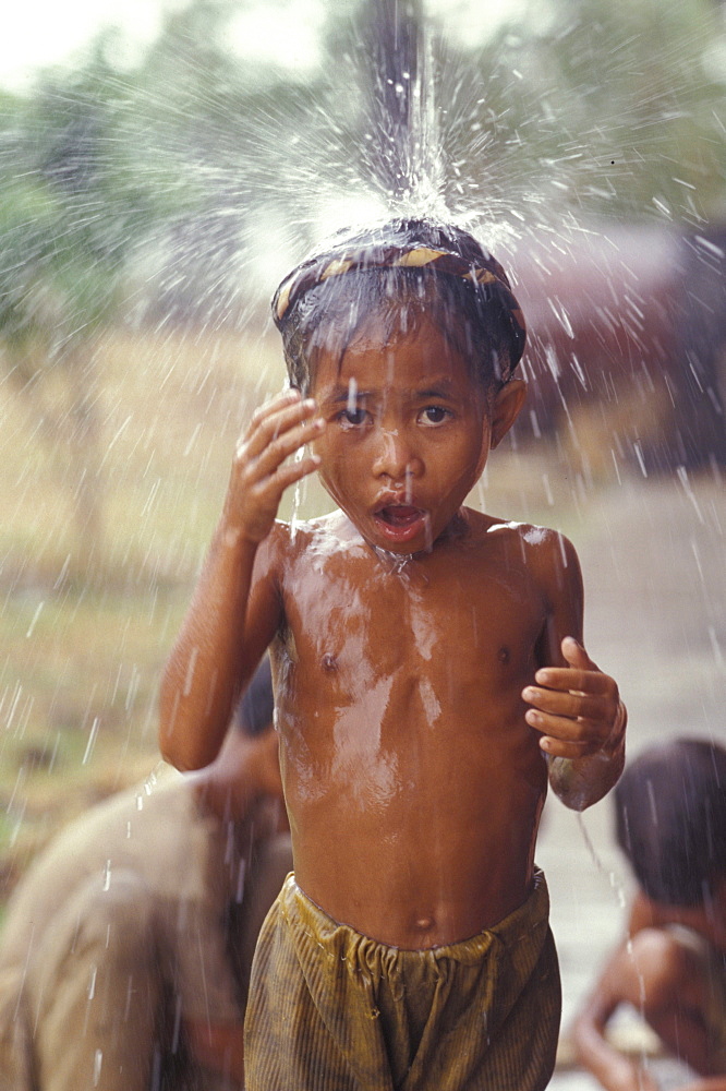 Cambodia taking a shower under a gutter overflow during a rainstorm. Takeo.