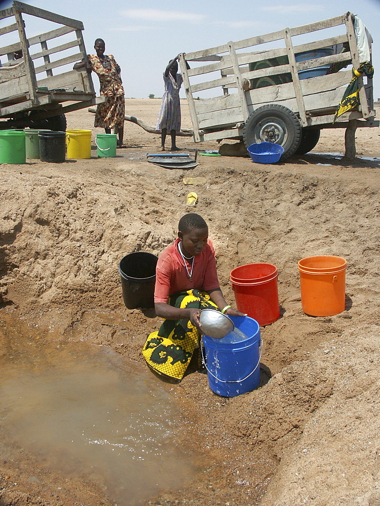 Woman collecting water from a dirty well in a dried up river bed, tanzania. near shinyanga