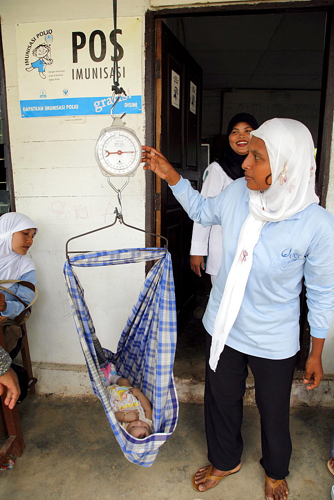 Indonesia growth monitoring (baby weighing) at a posyandu, or mother-child temporary health post in village of paya lumpat. Photograph taken in meulaboh, aceh province -december 2006, 2 years after tsunami of december 26th 2004 devastated much of coastal region. Taken to illustrate reconstruction work projects of (catholic relief services) of sponsored photo tour 