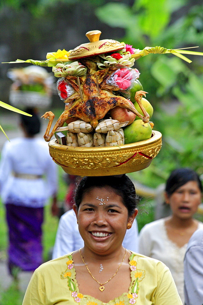 Indonesia woman walking along road carrying food offerings to temple, on hedr head, during hindu ceremony near klungkung on full moon. Bali 