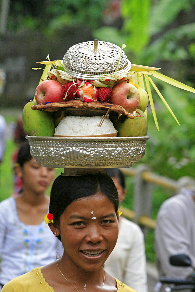 Indonesia woman walking along road carrying food offerings to temple, on hedr head, during hindu ceremony near klungkung on full moon. Bali 