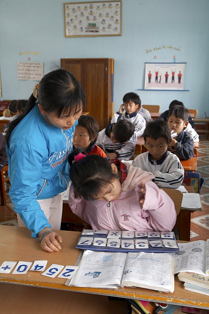 Vietnam yen mo tu commune primary school, ninh binh province. this is one of several schools in this region of northern vietnam where crs in cooperation with the local education authorities has implemented inclusive education practices, whereby children with mental or physical disabilities are integrated into the normal primary schools. crs provides special training for the teachers to help them. the image shows 13-year-old pham thi bich ngoc (in pink jacket) who suffers from cerebral palsy and is intergrated into a class of 11-year-olds. her teacher nguyen thi mund is seen here helping her with an alphabet exercise