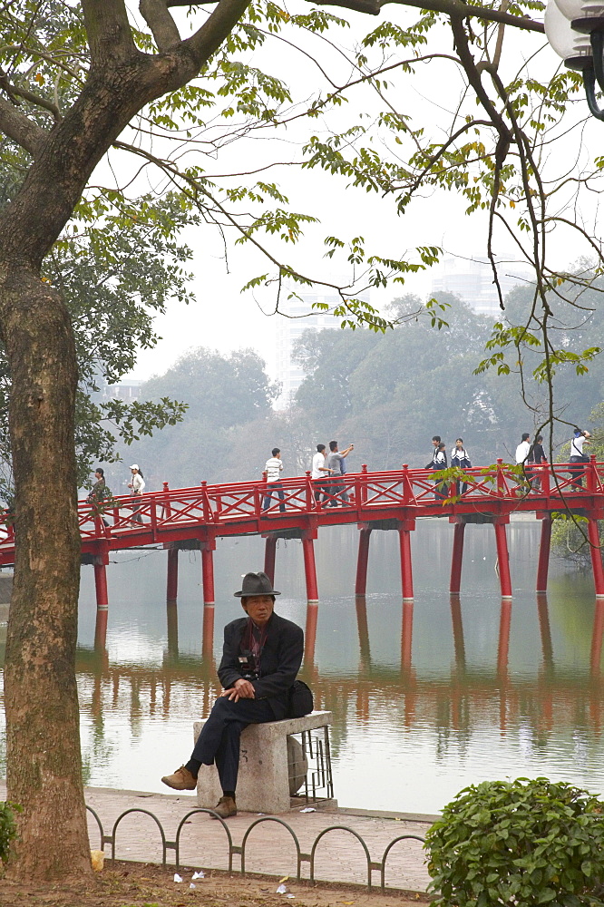 Vietnam people relaxing besdie hoan kiem lake, bridge to ngoc son temple in background, hanoi