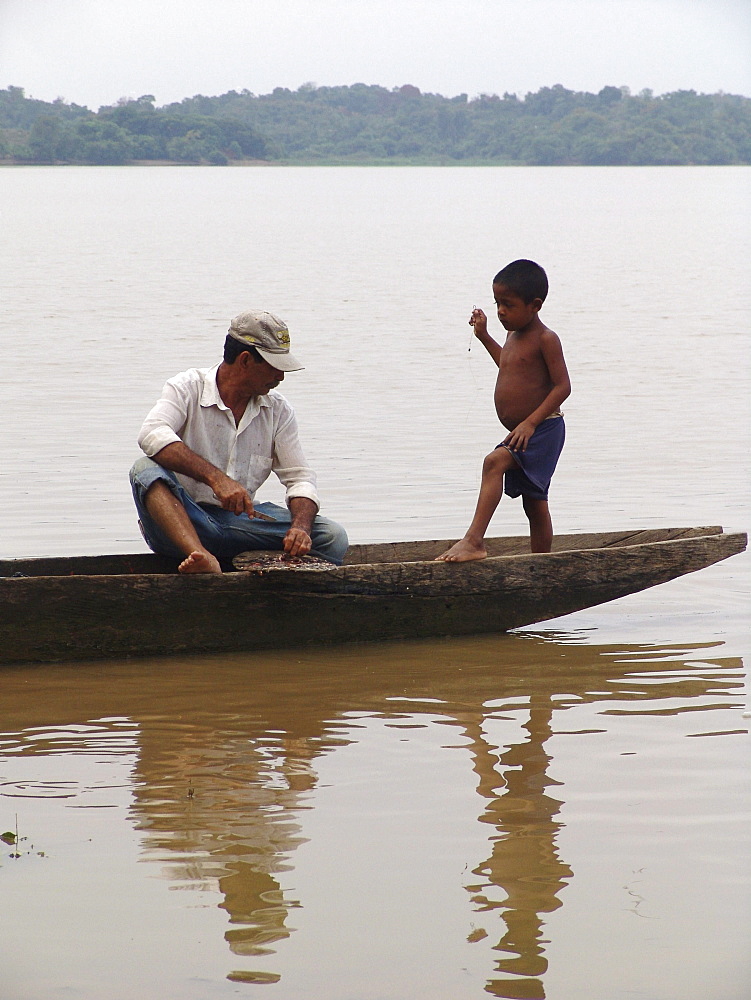 Colombia father and son fishing from a dugout canoe in the rio magdalena, barrancabermeja