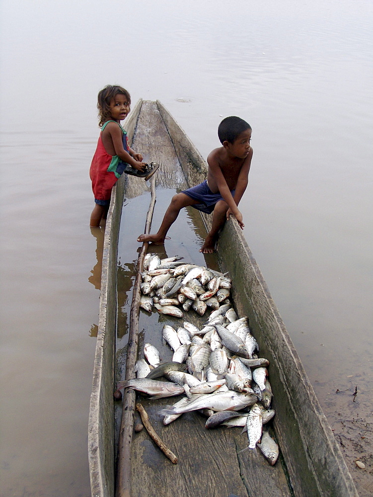 Colombia children sitting in a dug out canoe with fish. Rio magdalena, barrancabermeja