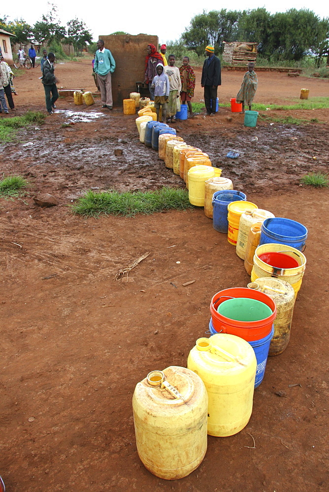 Tanzanian line of buckets waiting to be filled by a slow tap at a water distribution point in kansay, near ngorongoro. They will carry the bucket of water upto 3 miles each way to and from their homes.They And their families suffer from parasites and intestinal complaints because of the contaminated water