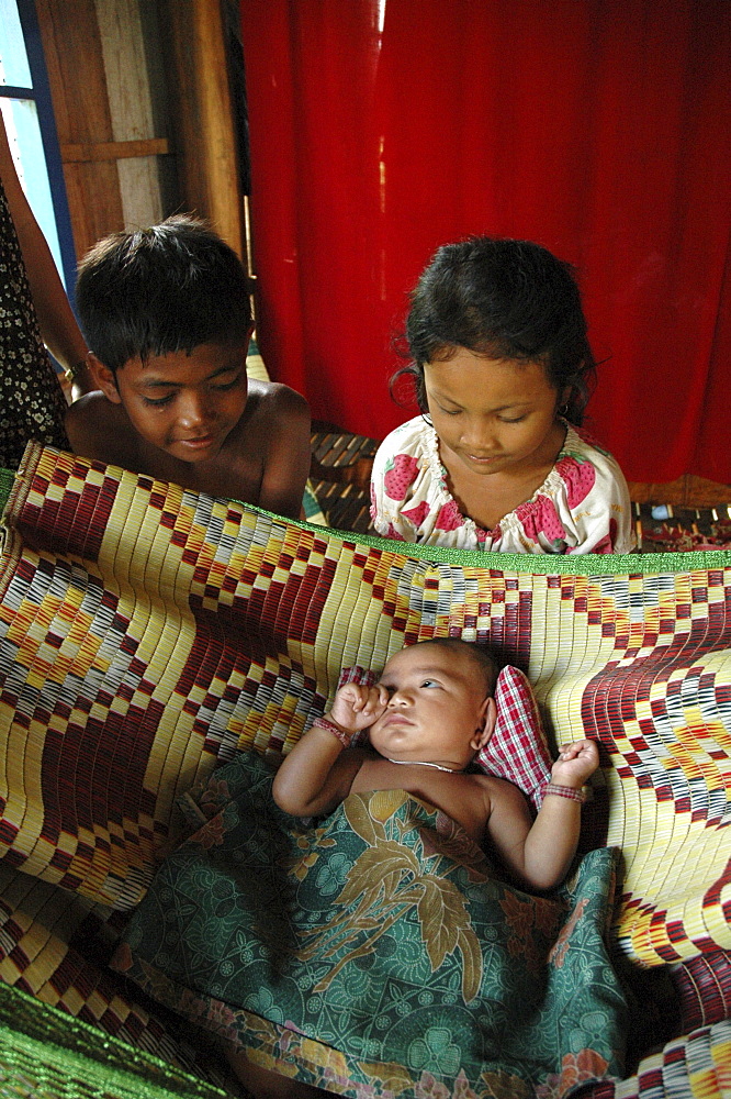 Cambodia girl and boy with their baby brother in hammock. Trac village, kampong cham