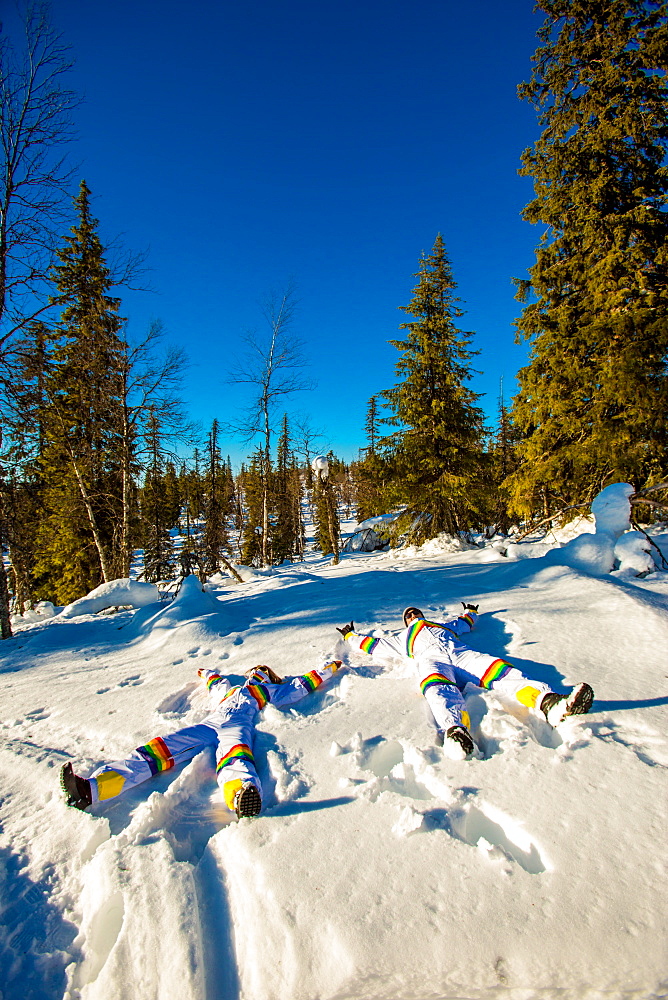 Couple doing snow angels wearing matching Rainbow Ski Suits, Kakslauttanen Igloo West Village, Saariselka, Finland, Scandinavia, Europe