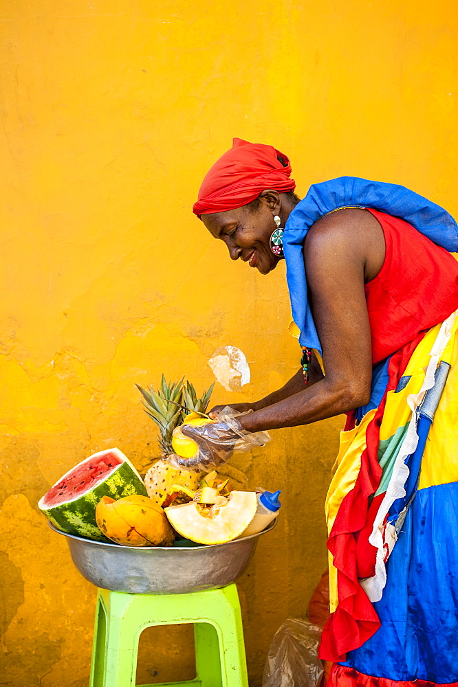 Woman dressed in traditional clothes cutting and selling fruit in the colorful old town of Cartagena, Colombia, South America