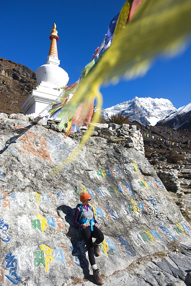 A woman trekking in the Langtang valley stops near a colorful Mani Stone wall below a Stupa decorated with Buddhist prayer flags, Langtang Region, Himalayas, Nepal, Asia