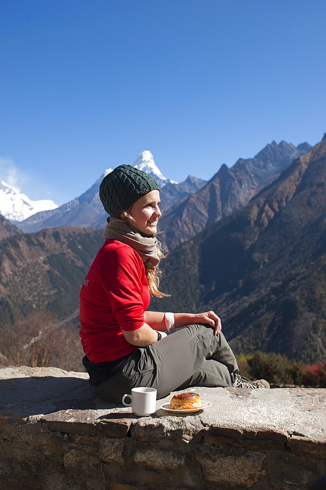 A trekker stops on the trail for some fuel, with Ama Dablam is the peak visible in the distance, Khumbu Region, Nepal, Asia