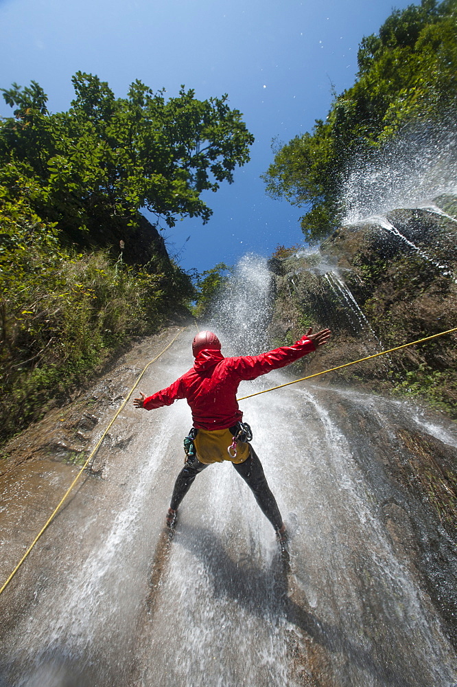 A man pauses to hold his arms in the falling water while canyoning, Nepal, Asia