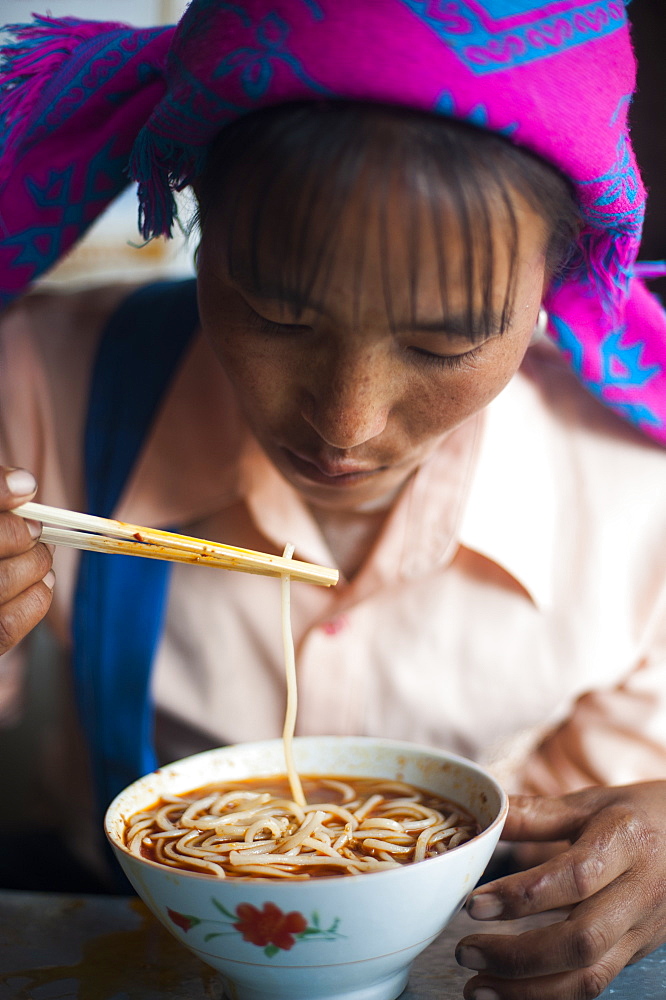 A Miao woman eats a bowl of noodles in Yunnan Province, China, Asia