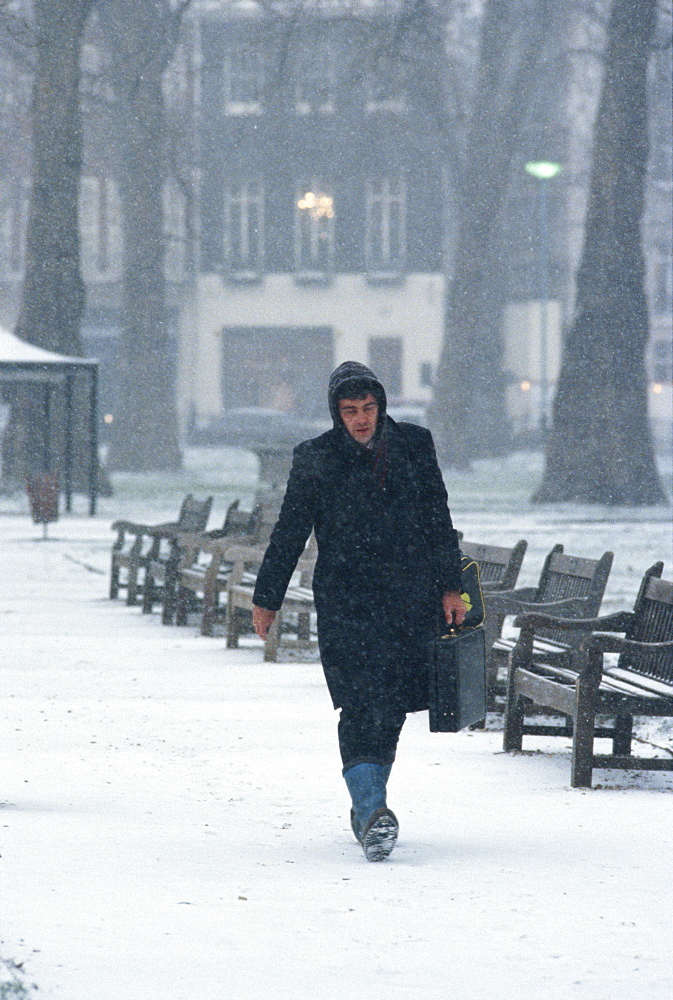 Man in boots and carrying a briefcase walks through snow in Berkeley Square in London, England, United Kingdom, Europe