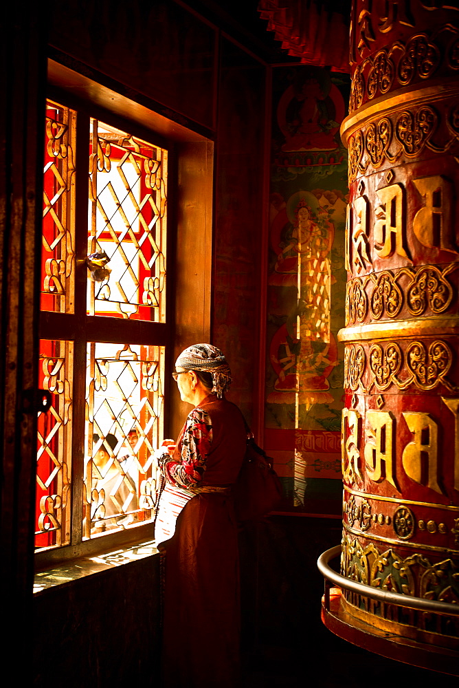 A Tibetan woman stands next to a large prayer wheel of the temple of Boudhanath Stupa, Kathmandu, Nepal, Asia