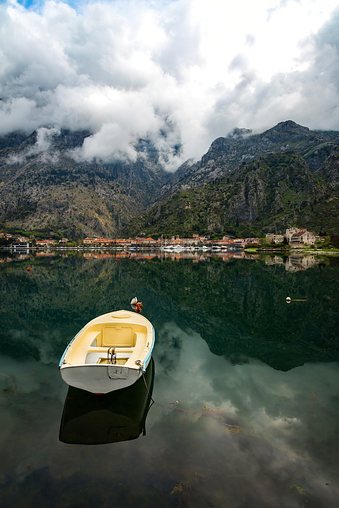 A small fishing boat sits in the reflection of the Old Town (stari grad) of Kotor in Kotor Bay, UNESCO World Heritage Site, Montenegro, Europe