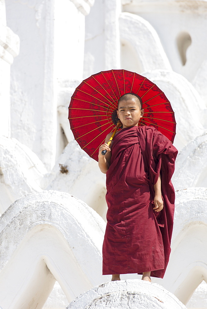 Young monk dressed in red, with red parasol at the Myatheindan Pagoda (White Temple) in Mingun, Myanmar (Burma), Asia