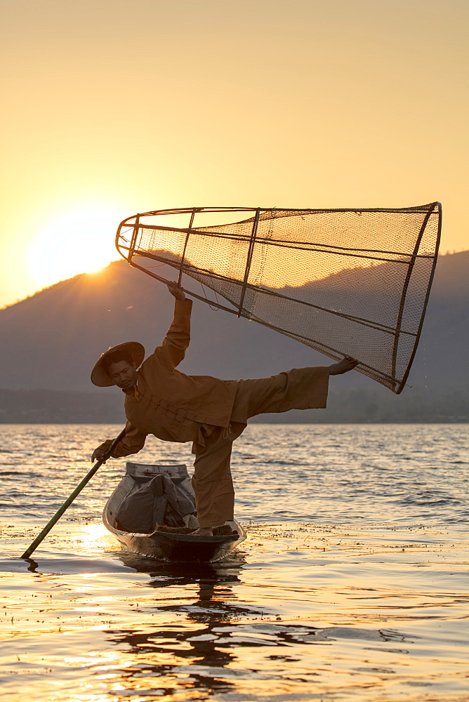 A fisherman standing on one leg and holding his fishing net at sunset on Inle Lake, Shan State, Myanmar (Burma), Asia