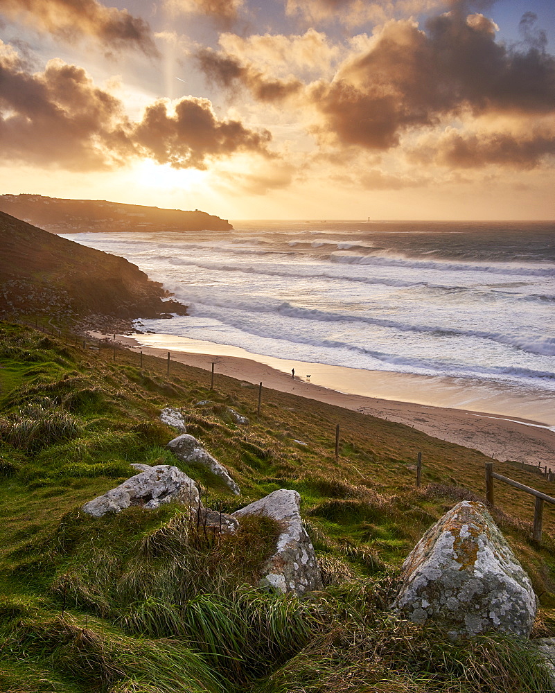 A winter dog walker watches the waves in a gale on the beach Gwenver near Sennen in Cornwall, England, United Kingdom, Europe