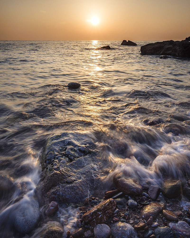 A colourful sunrise over Torbay with warm light glinting off the wave and wet rocks, Anstey's Cove, Torquay, Devon, England, United Kingdom, Europe