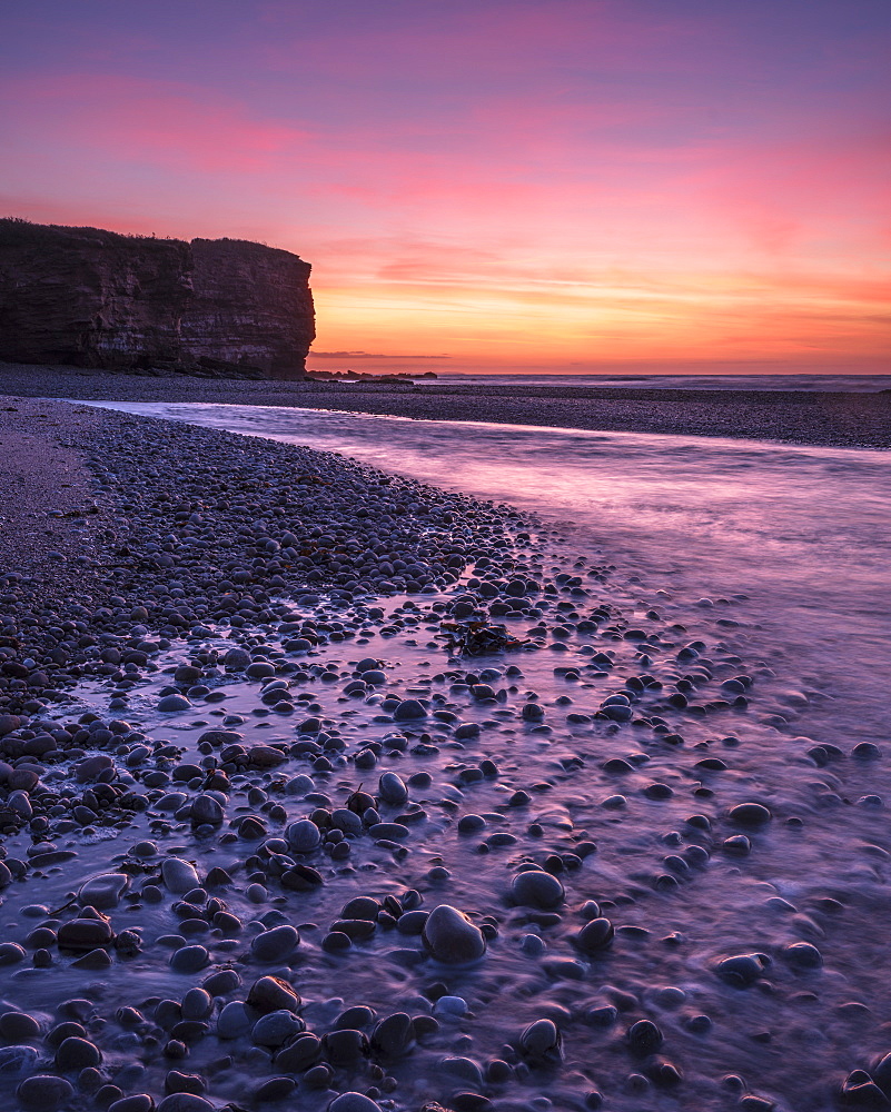 The River Otter meets the sea with strong dawn colour, wet pebbles and the cliff of Otter Head at Budleigh Salterton, Devon, England, United Kingdom, Europe