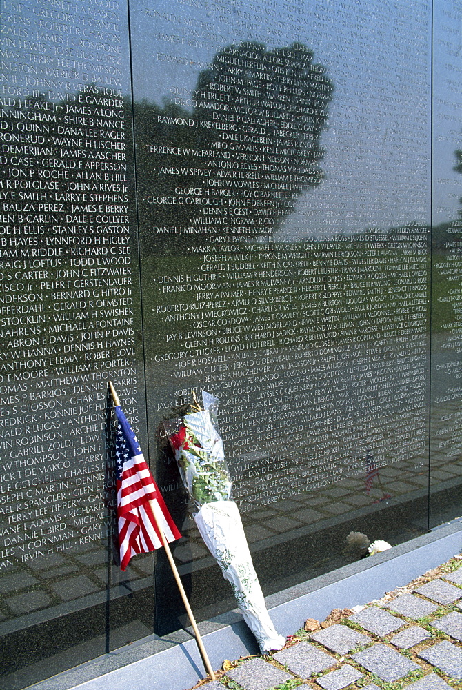 Flag and flowers against the list of names on the Vietnam Veterans Memorial in Washington D.C., United States of America, North America